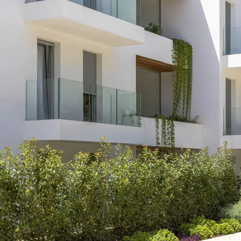 White Mediterranean apartment building with glass balconies and greenery
